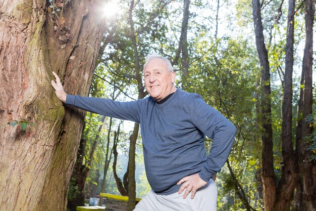 Sonriendo hombre descansando con su mano en un árbol