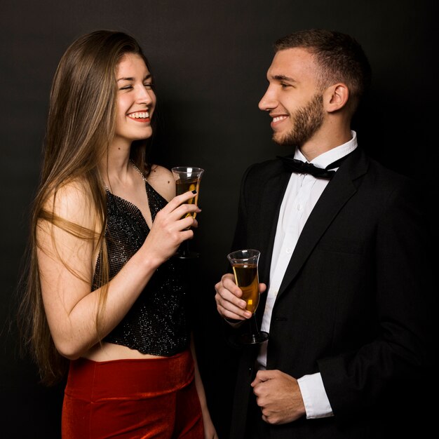 Sonriendo el hombre y la mujer en la chaqueta de la cena y ropa de noche con vasos de bebidas