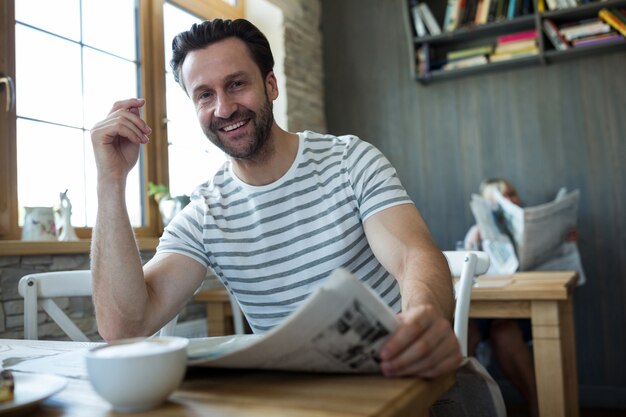 Sonriendo hombre sentado con un periódico en una cafetería