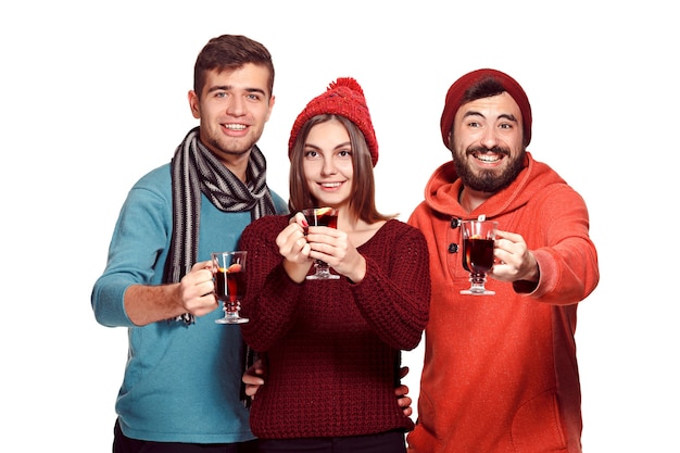 Sonriendo a hombres y mujeres europeos durante la sesión de fotos del partido. Los chicos se hacen pasar por amigos en el festival de estudio con copas con vino caliente caliente en primer plano.