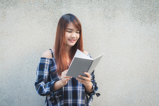 Sonriendo jóvenes hermosas mujeres asiáticas con el libro. Closeup cabeza de color marrón hermosa joven bastante feliz lectura sobre fondo de muro de hormigón. Vintage efecto estilo imágenes.