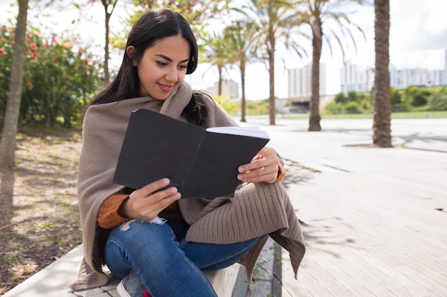 Sonriendo el libro bonito de la lectura de la mujer y estudiando al aire libre