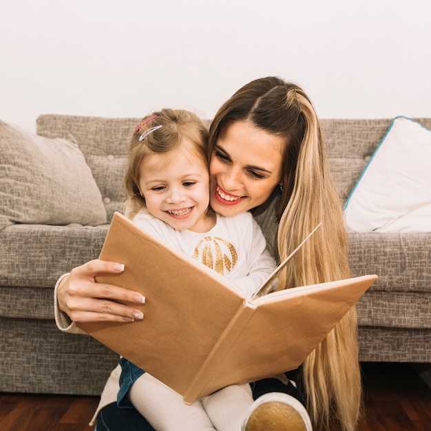 Sonriendo el libro de lectura de madre e hija cerca del sofá