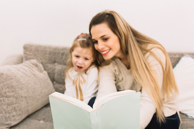 Sonriendo el libro de lectura de la madre con la hija en el sofá