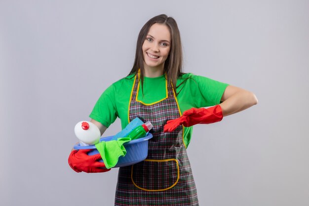 Sonriendo limpieza joven vestida de uniforme en guantes rojos puntos en herramientas en su mano sobre fondo blanco aislado