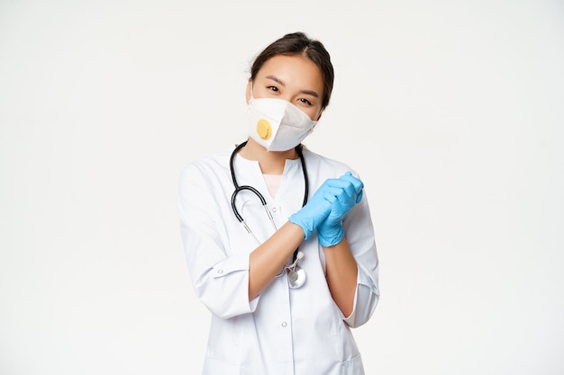 Sonriendo lindo asiático mujer médico enfermera en respirador médico y guantes de goma estériles buscando súplicas ...