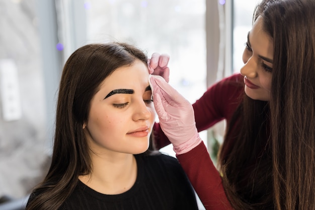 Sonriendo el maestro de cejas haciendo su mejor procedimiento de maquillaje