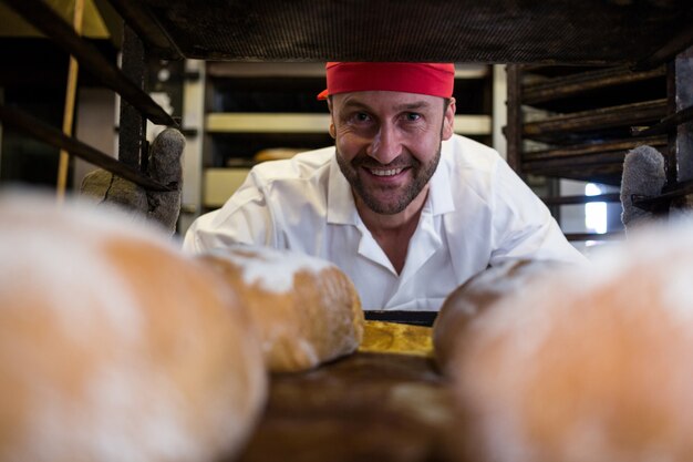 Sonriendo manteniendo la bandeja de bollos al horno panadero en estantería