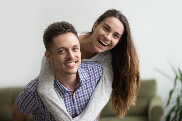 Sonriendo marido piggybacking alegre esposa en casa, feliz pareja retrato