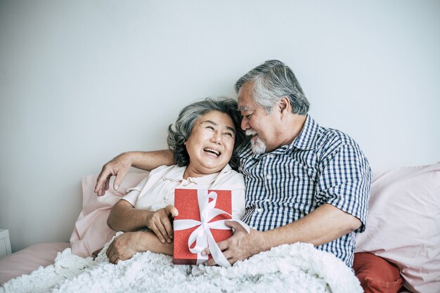 Sonriendo marido senior haciendo sorpresa dando caja de regalo a su esposa en el dormitorio