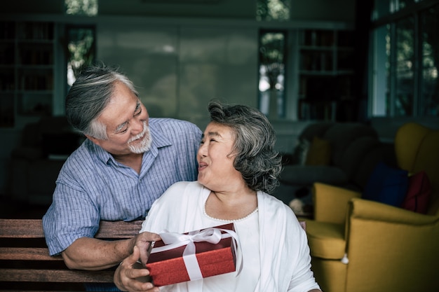 Sonriendo marido senior haciendo sorpresa dando caja de regalo a su esposa