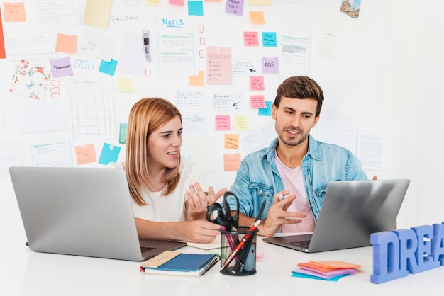 Sonriendo masculino y femenino sentado en el escritorio y hablando mirando portátil