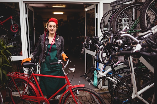 Sonriendo mecánico permanente con una bicicleta en el taller