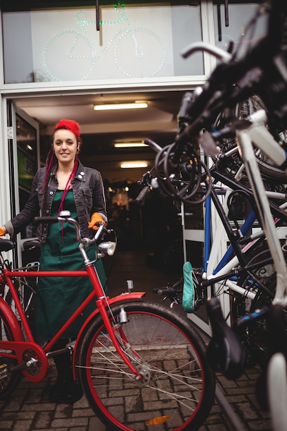 Sonriendo mecánico permanente con una bicicleta en el taller