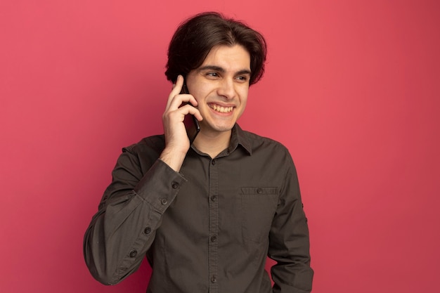 Sonriendo mirando al lado chico guapo joven con camiseta negra habla por teléfono aislado en la pared rosa