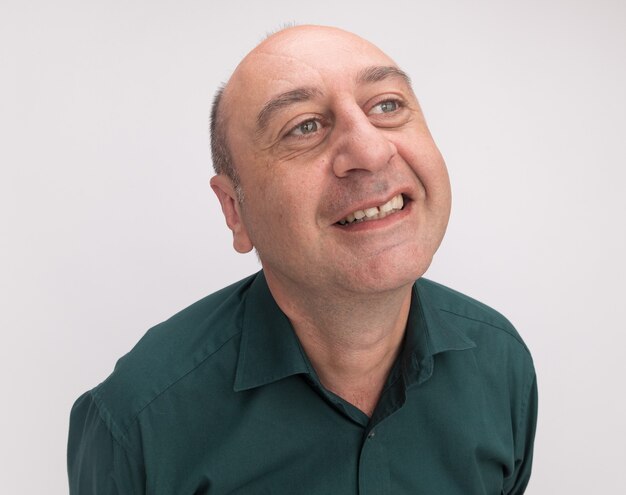 Sonriendo mirando al lado hombre de mediana edad vestido con camiseta verde aislado en la pared blanca