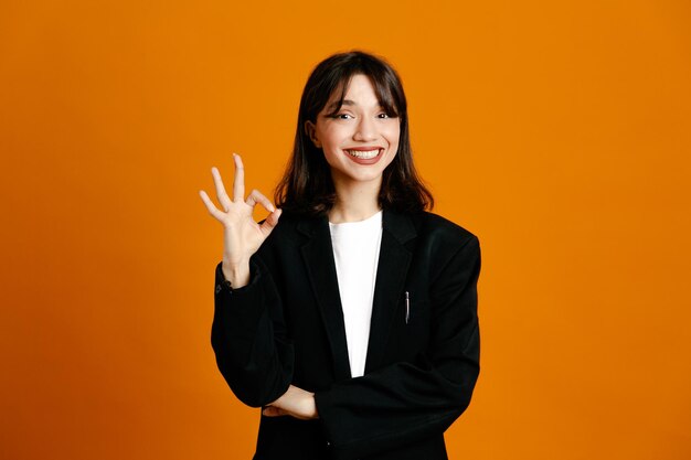 Sonriendo mostrando bien gesto joven hermosa mujer vistiendo chaqueta negra aislado sobre fondo naranja