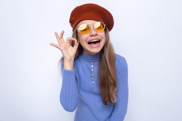 Sonriendo mostrando gesto bien hermosa niña con gafas con sombrero aislado en la pared blanca