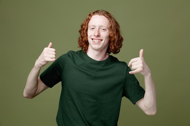 Sonriendo mostrando los pulgares hacia arriba joven guapo con camiseta verde aislado sobre fondo verde