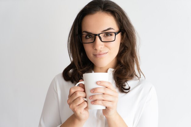 Foto gratuita sonriendo a la mujer bastante joven que sostiene la taza y que mira la cámara.