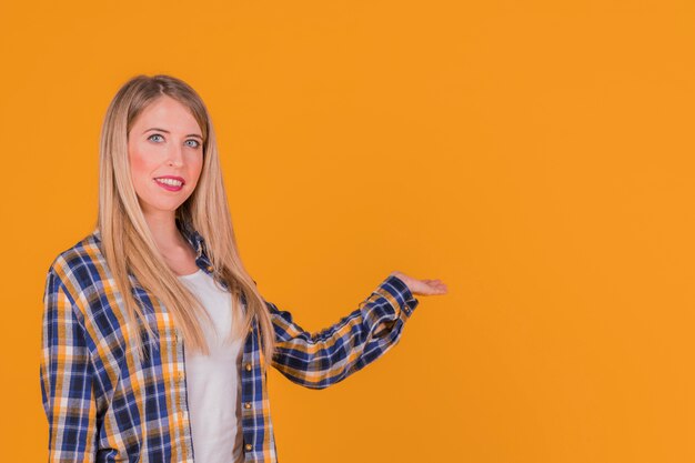 Sonriendo a una mujer joven que presenta algo contra un fondo naranja