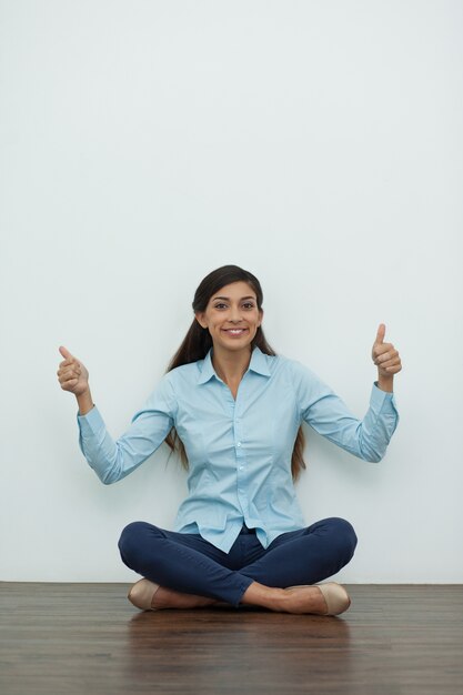 Sonriendo Mujer sentada en el suelo con los pulgares para arriba