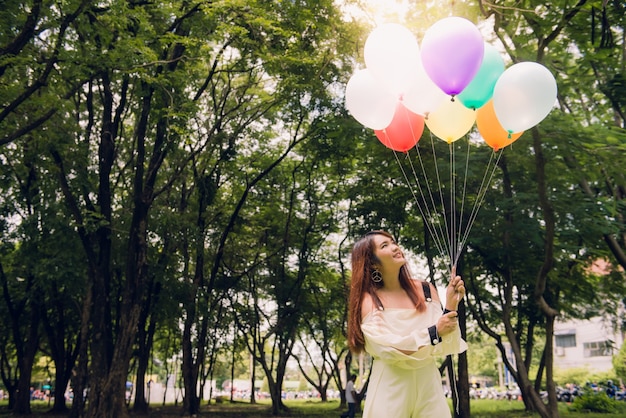 Foto gratuita sonriendo a las mujeres asiáticas hermosas jovenes con el pelo marrón largo en el parque. con los globos de aire de color arco iris en sus manos. una energía positiva y natural de la naturaleza.