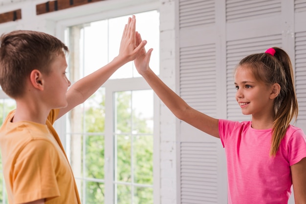 Sonriendo niño y niña dando alta cinco cerca de la ventana