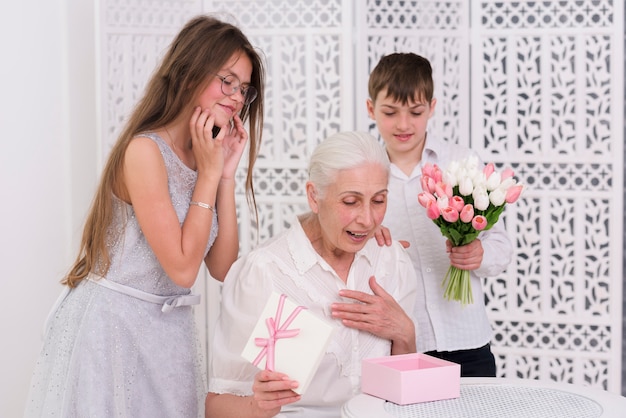 Sonriendo el niño y la niña de pie detrás de la abuela sorprendida