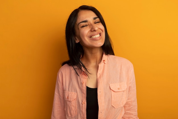 Sonriendo con los ojos cerrados hermosa joven vestida con camiseta rosa aislada en la pared amarilla