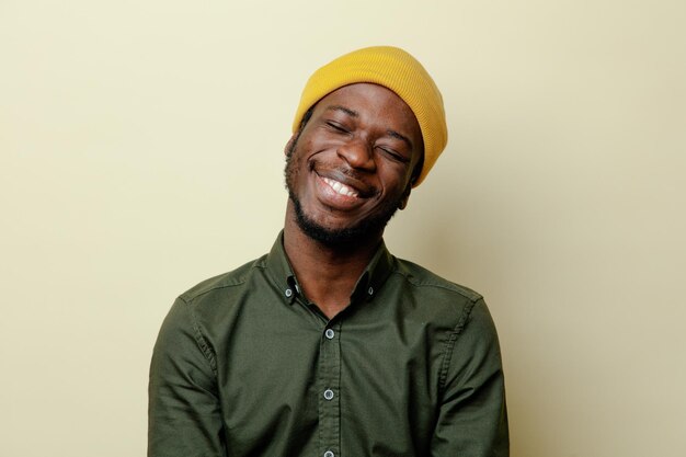 Sonriendo con los ojos cerrados joven afroamericano con sombrero con camisa verde aislado sobre fondo blanco.