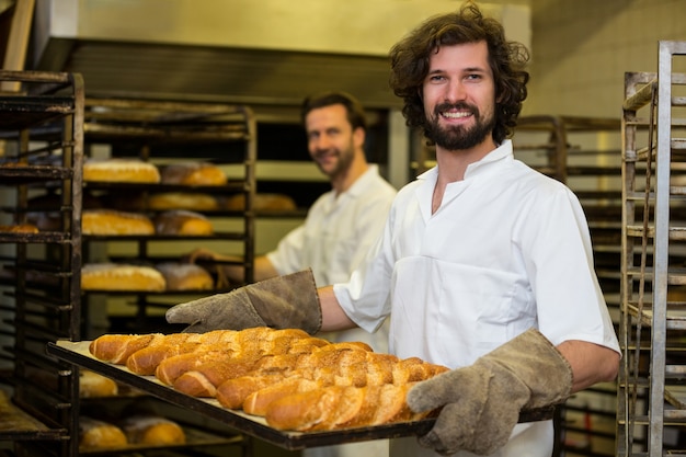 Sonriendo panadero con una bandeja de barra de pan francés recién horneado