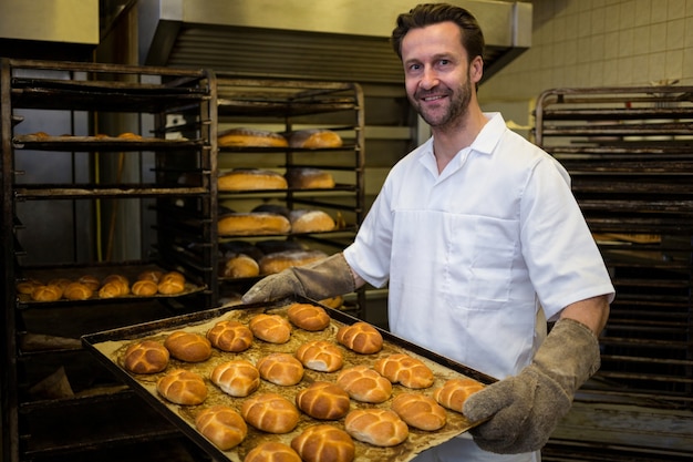 Sonriendo panadero con una bandeja de bollos horneados