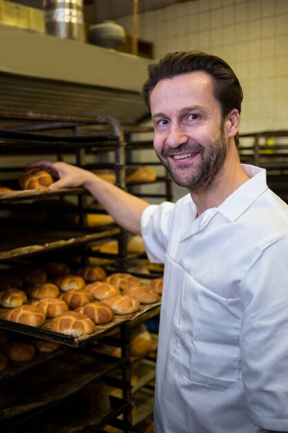 Sonriendo panadero colocación de bollos al horno en estante