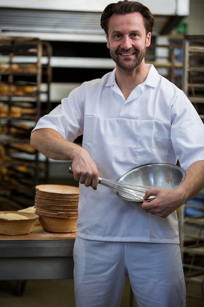 Foto gratuita sonriendo panadero que sostiene un cuenco y un batidor