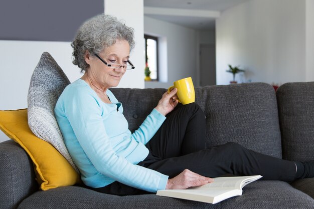 Sonriendo positiva jubilada señora emocionada con novela interesante