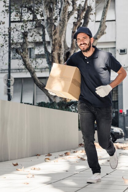 Sonriendo repartidor corriendo sobre el pavimento con paquete