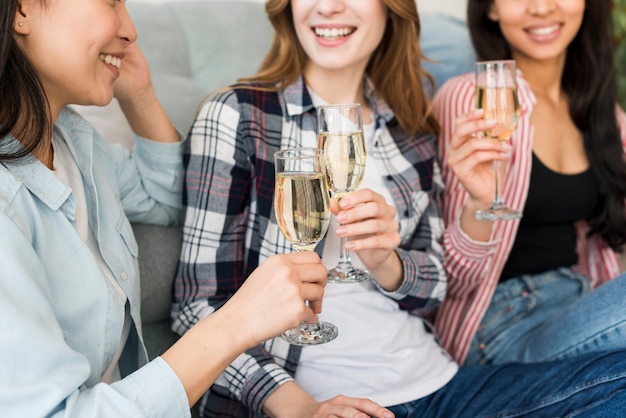 Sonriendo y sentándose en el sofá mujeres bebiendo champán