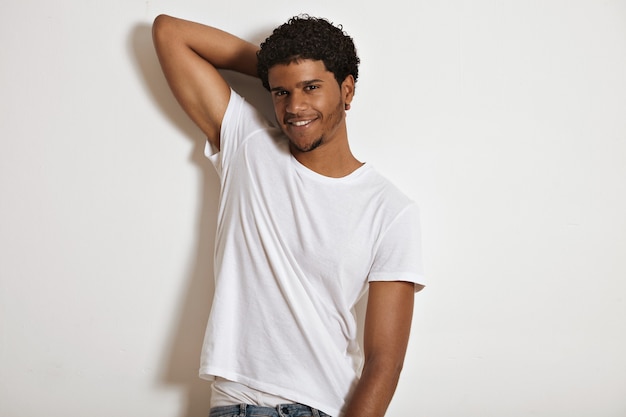 Sonriendo sexy modelo afroamericano con una camiseta blanca de algodón en blanco levantando la mano haciendo que su ropa interior blanca se muestre de jeans