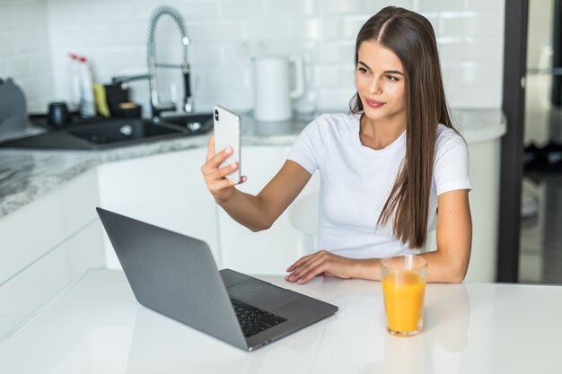 Sonriendo videollamada de mujer joven en el teléfono en la cocina