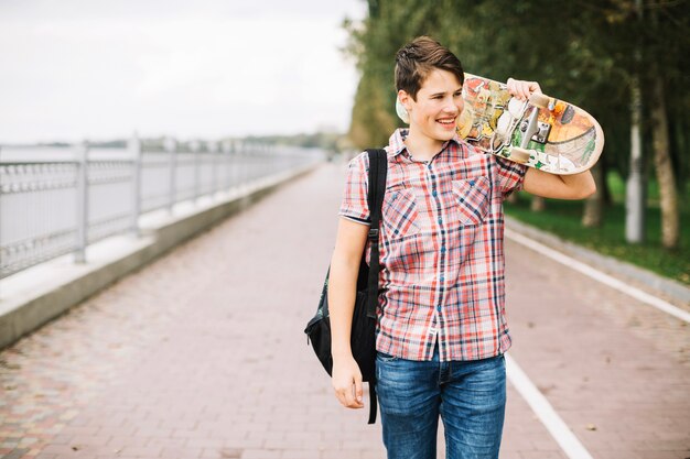 Sonriente adolescente con patineta en el hombro