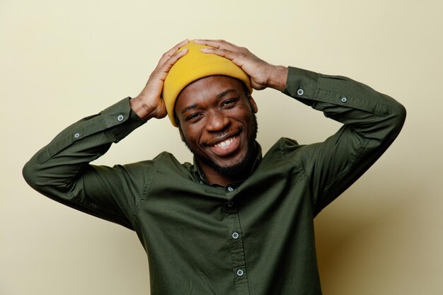 Sonriente agarró la cabeza del joven afroamericano con sombrero y camisa verde aislada en el fondo blanco