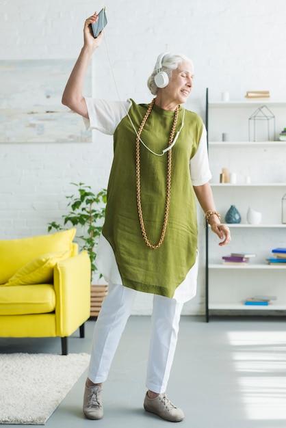 Foto gratuita sonriente anciana escuchando música en auriculares bailando en casa