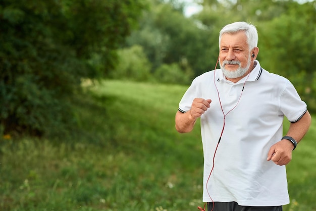 Sonriente anciano corriendo en el parque de la ciudad verde