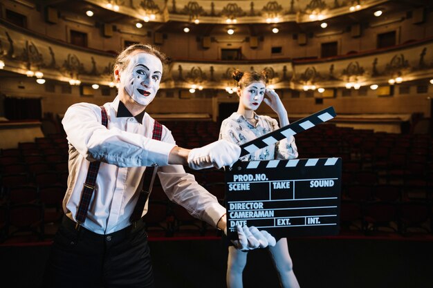 Sonriente artista mime hombre sosteniendo claqueta frente a mime femenino en el escenario