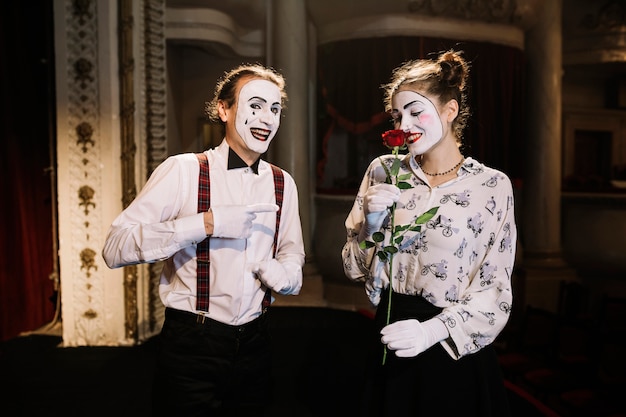 Foto gratuita sonriente artista de mimo masculino apuntando al mimo femenino que huele a rosa roja