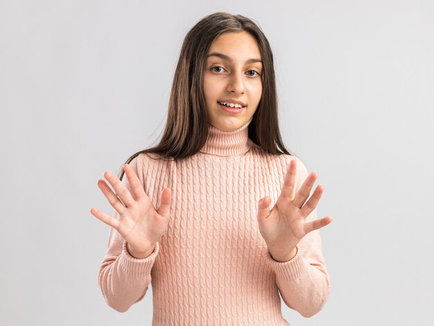 Sonriente a bastante adolescente mirando al frente mostrando las manos vacías aisladas en la pared blanca con espacio de copia