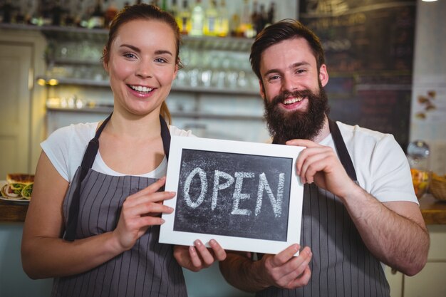 sonriente camarera y el camarero coloca con la tarjeta muestra abierta en el café