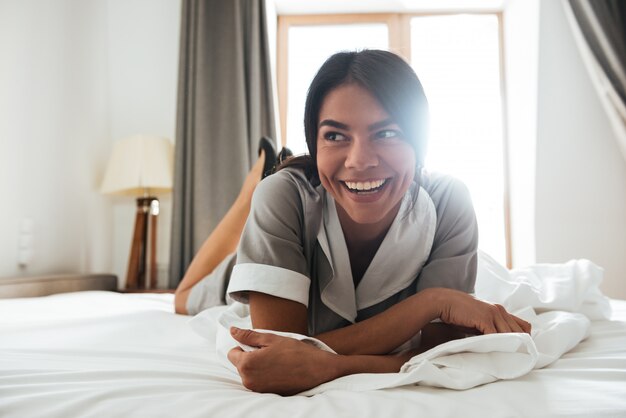 Sonriente camarera del hotel acostada en una cama