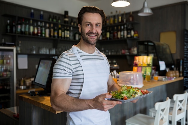 Sonriente camarero con una bandeja de ensalada en el restaurante